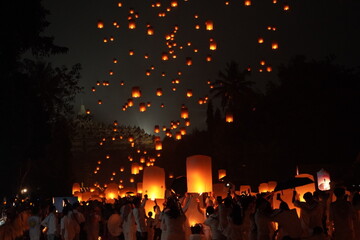 A group of people are holding lit lanterns and flying them in the air during Vesak Day. © Reezky