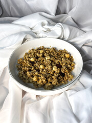 Granola with nuts and raisins in a white plate close-up on a white textile background. Top view. Healthy proper breakfast.