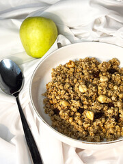 Granola with nuts and raisins in a white plate close-up on a white textile background. Top view. Healthy proper breakfast.