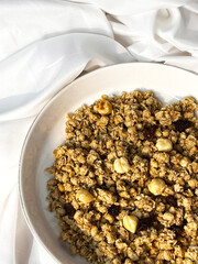 Granola with nuts and raisins in a white plate close-up on a white textile background. Top view. Healthy proper breakfast.