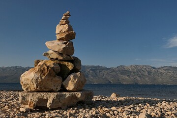 Stone cairn created on rocky beach north of Razanac, northern Dalmatia, Croatia. Bay water and...
