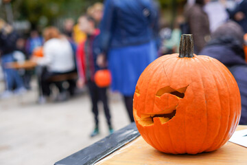 a carved pumpkin with a partially broken face, placed on a table outdoors, with a blurred...