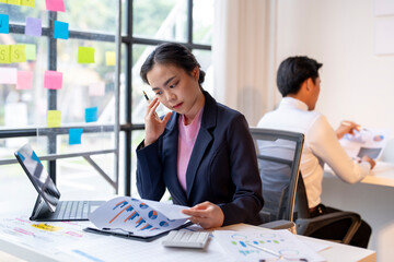 A woman in a suit is talking on her cell phone while looking at a piece of paper