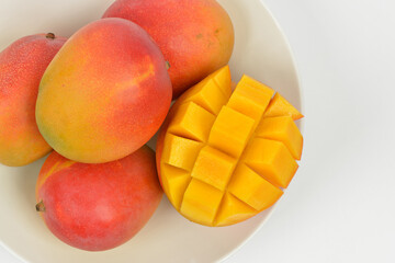 Close-up and top angle view of stacked red Apple Mangos and one half cut with yellow flesh in a white dish on white floor, South Korea