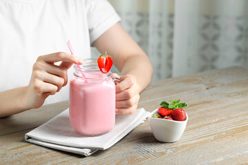 Woman with mason jar of tasty strawberry yogurt at wooden table, closeup