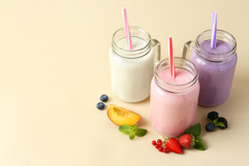Different tasty yogurts in mason jars, peach, fresh berries and mint on pale yellow background, space for text