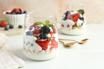 Tasty yogurt with fresh berries, granola and mint in glasses served on white table