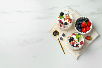 Tasty yogurt with fresh berries, granola and mint in glasses served on white table, flat lay. Space for text