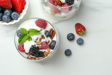 Tasty yogurt with fresh berries, granola and mint in glasses on white table, flat lay