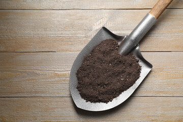 Metal shovel with soil on light wooden table, top view. Space for text