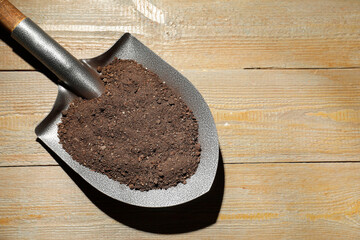 Metal shovel with soil on wooden table, top view. Space for text