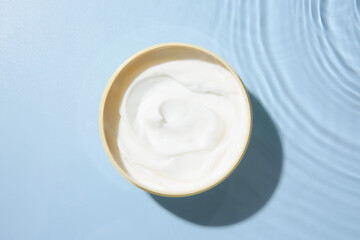 Cosmetic product. Jar with cream in water on light blue background, top view