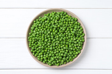 Fresh green peas in plate on white wooden table, top view