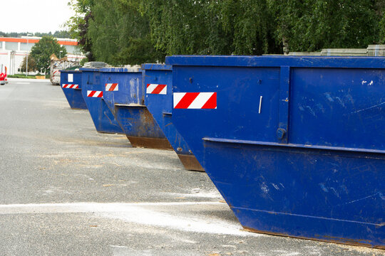 Row of large blue industrial waste containers lined up along an asphalt road in an urban area