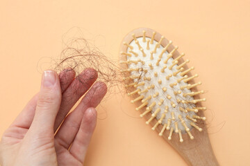 Woman taking her lost hair from brush on beige background, top view