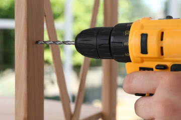 Man with electric screwdriver assembling furniture indoors, closeup