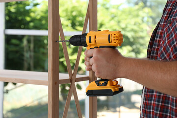 Man with electric screwdriver assembling furniture indoors, closeup