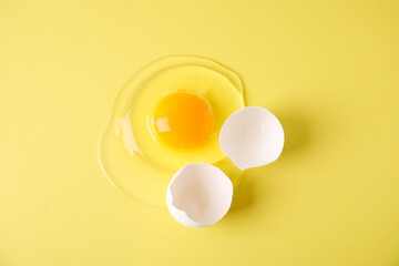 Broken raw egg and shell on yellow background, top view