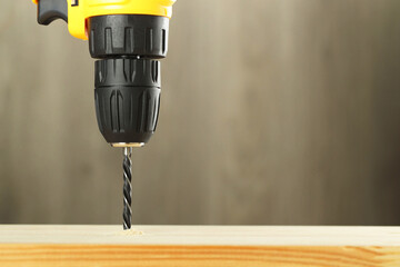 Drilling hole in wooden plank on grey background, closeup. Space for text