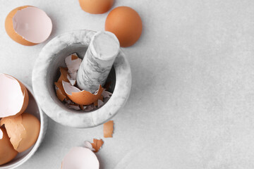 Broken eggshells, mortar and pestle on grey table, flat lay. Space for text
