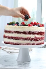 Woman decorating tasty sponge cake with berries at white marble table, closeup