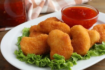 Tasty chicken nuggets with chili sauce and lettuce on table, closeup