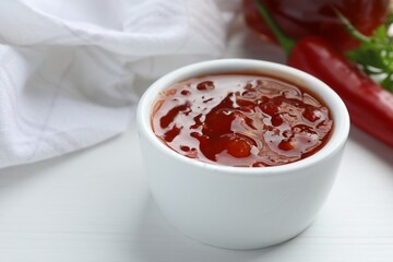 Spicy chili sauce in bowl on white wooden table, closeup