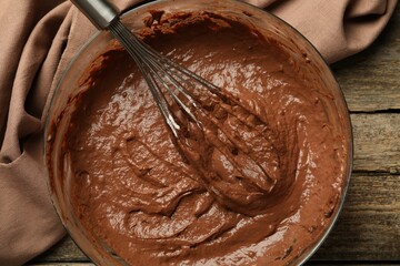Chocolate dough in bowl and whisk on wooden table, top view