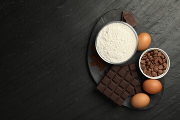 Flour, chocolate and eggs for making dough on dark textured table, top view. Space for text