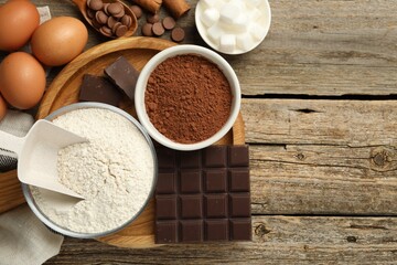 Flat lay composition with flour, chocolate and other ingredients for making dough on wooden table. Space for text
