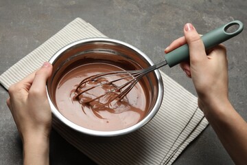 Woman mixing chocolate dough with whisk at grey table, closeup