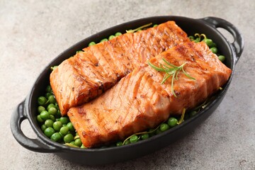 Delicious grilled salmon fillets with rosemary and green peas in baking dish on grey textured table, closeup