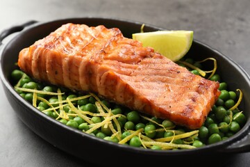 Delicious grilled salmon fillet with green peas and lime in baking dish on grey table, closeup