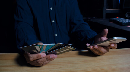 A man holds multiple credit cards in one hand and a smartphone in the other, glancing at the screen as he performs financial transactions, symbolizing the ease and mobility of managing finances throug