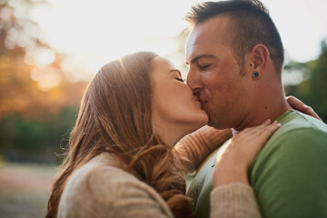 Fototapeta premium Nature, couple and love with kiss for relationship, connection and bonding together on date. Happy people, woman and man with hug for admiration, affection and commitment with security in Canada