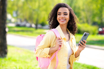 Portrait of attractive wavy hair cheerful girl enjoy good weather hold device pink blackpack wear yellow jacket having fun outside outdoors