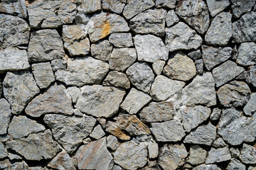 A wall made of stone with a grey color. The wall is made of many small stones. The wall is very rough and has a lot of texture