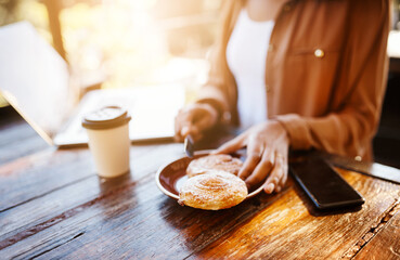 Hands, cafe and table with pastry, coffee and laptop for online meeting, remote work or relax. Person, tech and restaurant for breakfast, beverage and working as creative or digital nomad for agency