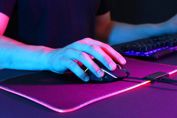 Gamer using modern wired computer mouse in neon lights at dark table, closeup © New Africa