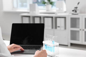 Doctor with laptop at table in clinic, closeup view