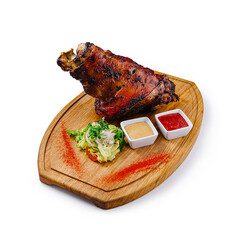 Roasted pork knuckle served on wooden board with sauces and salad
