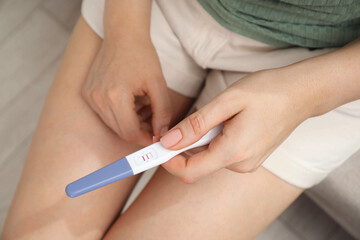 Woman holding positive pregnancy test indoors, closeup view