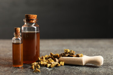 Honey tincture and scoop with propolis granules on grey textured table, closeup. Space for text