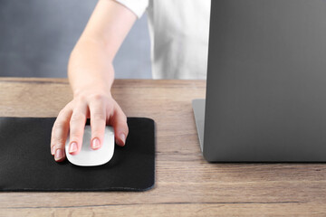 Fototapeta premium Woman using computer mouse while working with laptop at wooden table, closeup