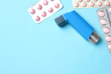 Asthma inhaler and pills on light blue background, flat lay. Space for text