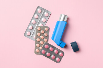 Asthma inhaler and pills on pink background, flat lay