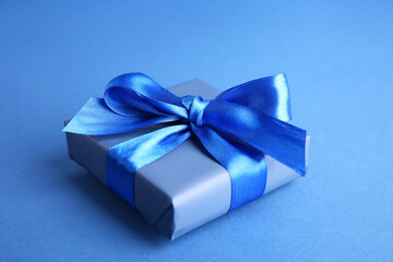 Gift box with satin bow on blue background, closeup