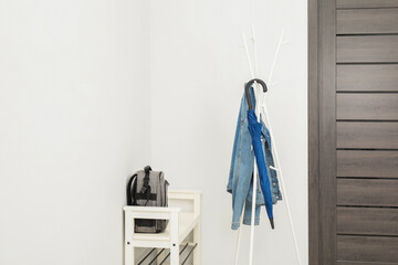 Blue umbrella and denim jacket on clothing rack near shoe storage bench with backpack in hallway