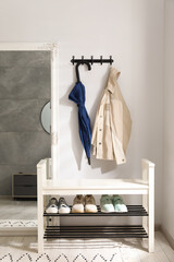 Blue umbrella and jacket on hanger near mirror over shoe storage bench indoors