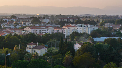 Fototapeta premium View of the city of Perpignan, France, sunset, haze, red roofs, houses, trees, life, vacation, postcard, Europe, mountain silhouettes, calm, beauty